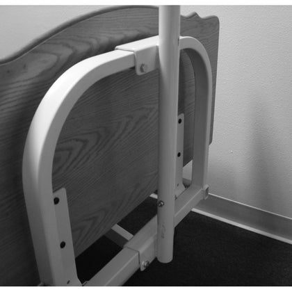 The Joerns trapeze adapter mounted at the head of a bed frame, with the trapeze bar post standing in it