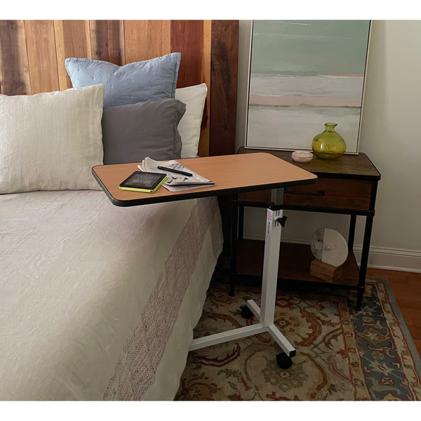 An overbed table with a tablet and a newspaper beside a made bed