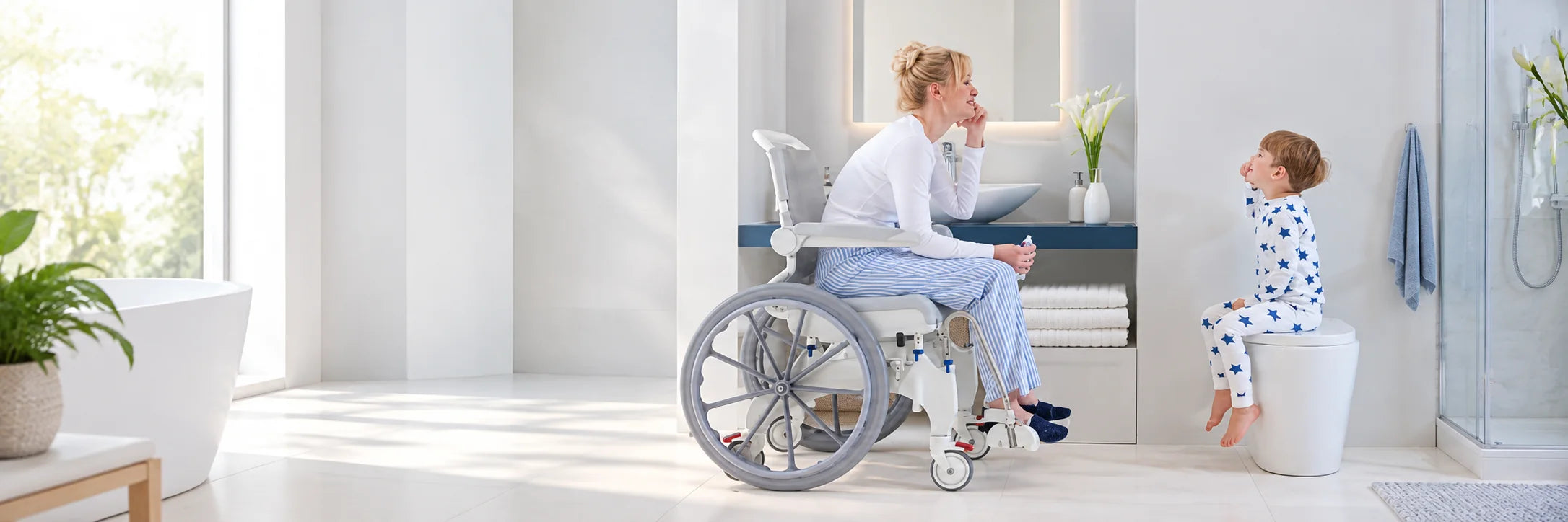 A woman in a shower commode wheelchair at the bathroom sink, smiling at a young boy in pajamas