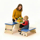 A toddler at an Axis bench used as a play table, with a parent on another Axis