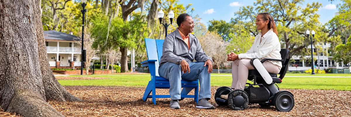 A man and a woman in a power wheelchair talking in a park