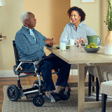 A man in a Journey Zoomer pulled up to a dining table with a companion