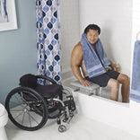 A wheelchair user seated on the Nuprodx MC3000 TX beside the tub