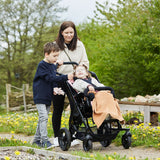 A mother pushing a girl in a Chilla on a park path, with her son holding the handle