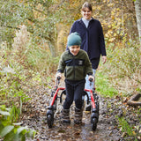 A boy walking on a muddy forest path in a Crocodile AT, with an adult behind him