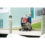 A man seated in a Merits Vision Sport power wheelchair outdoors beside a marina