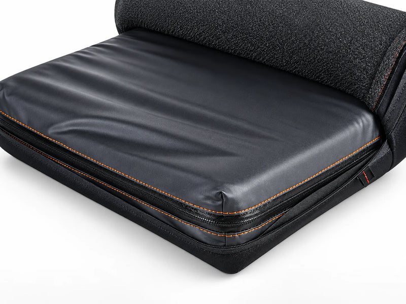 A black wheelchair cushion in its cover, with a fabric cover partly rolled back