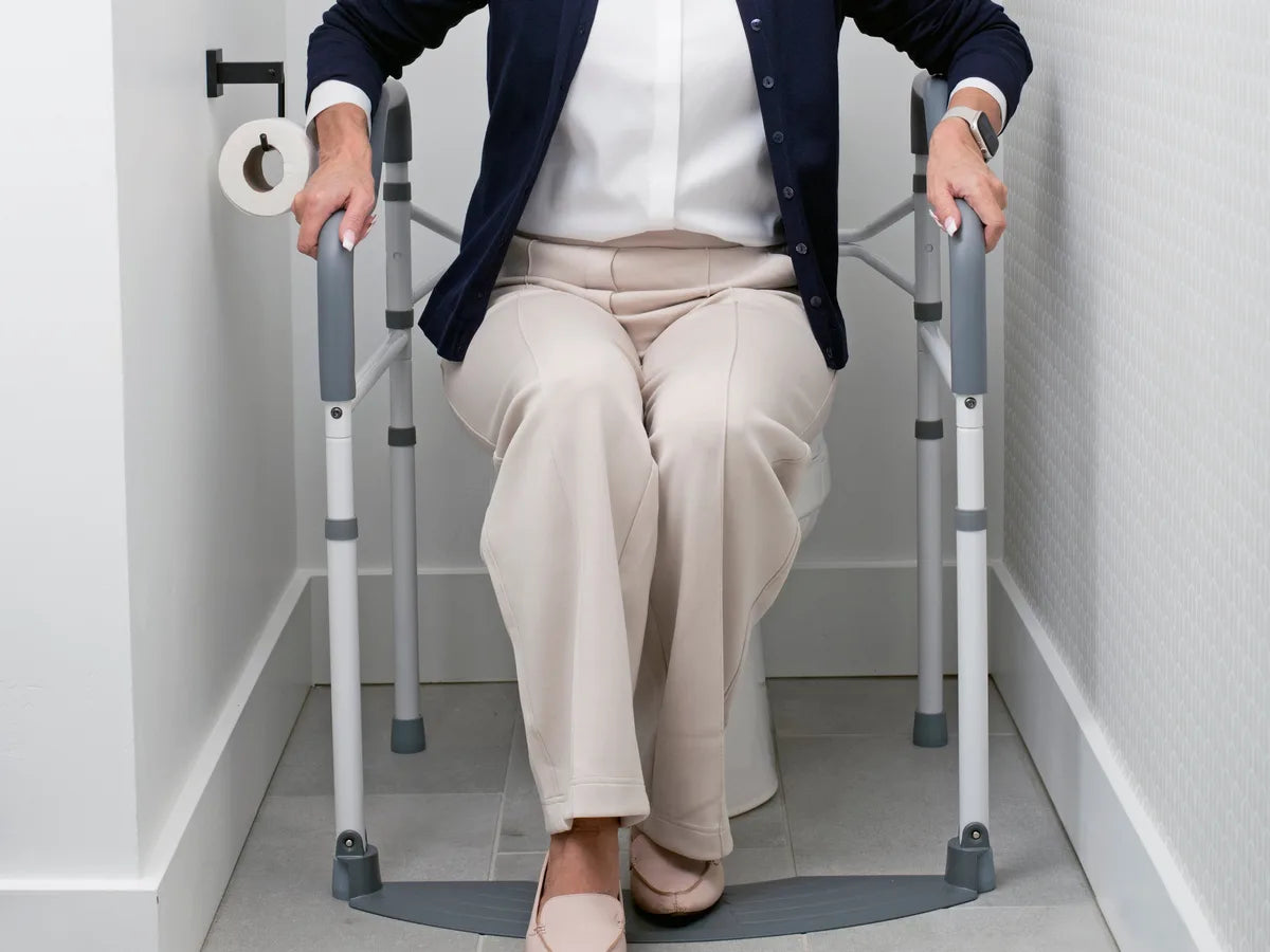 A woman seated on a toilet with her hands on the arm rests of a toilet safety frame