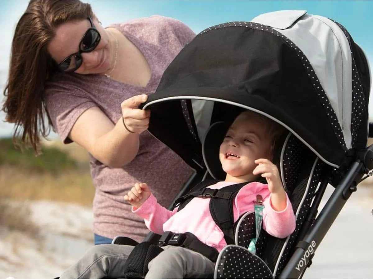 A mother adjusting the canopy over her smiling toddler in an adaptive stroller