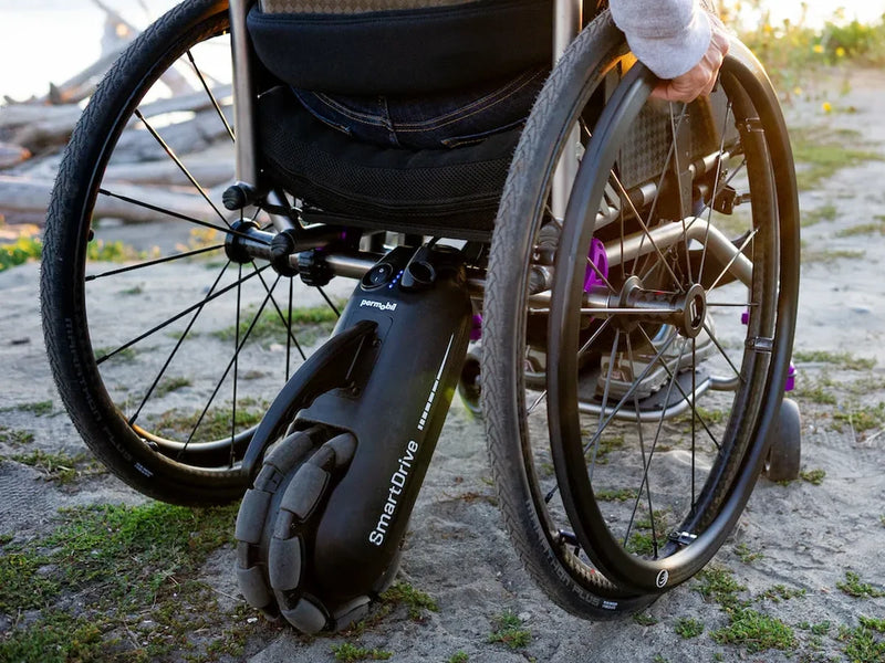 A power assist drive unit mounted under a manual wheelchair on a sandy path