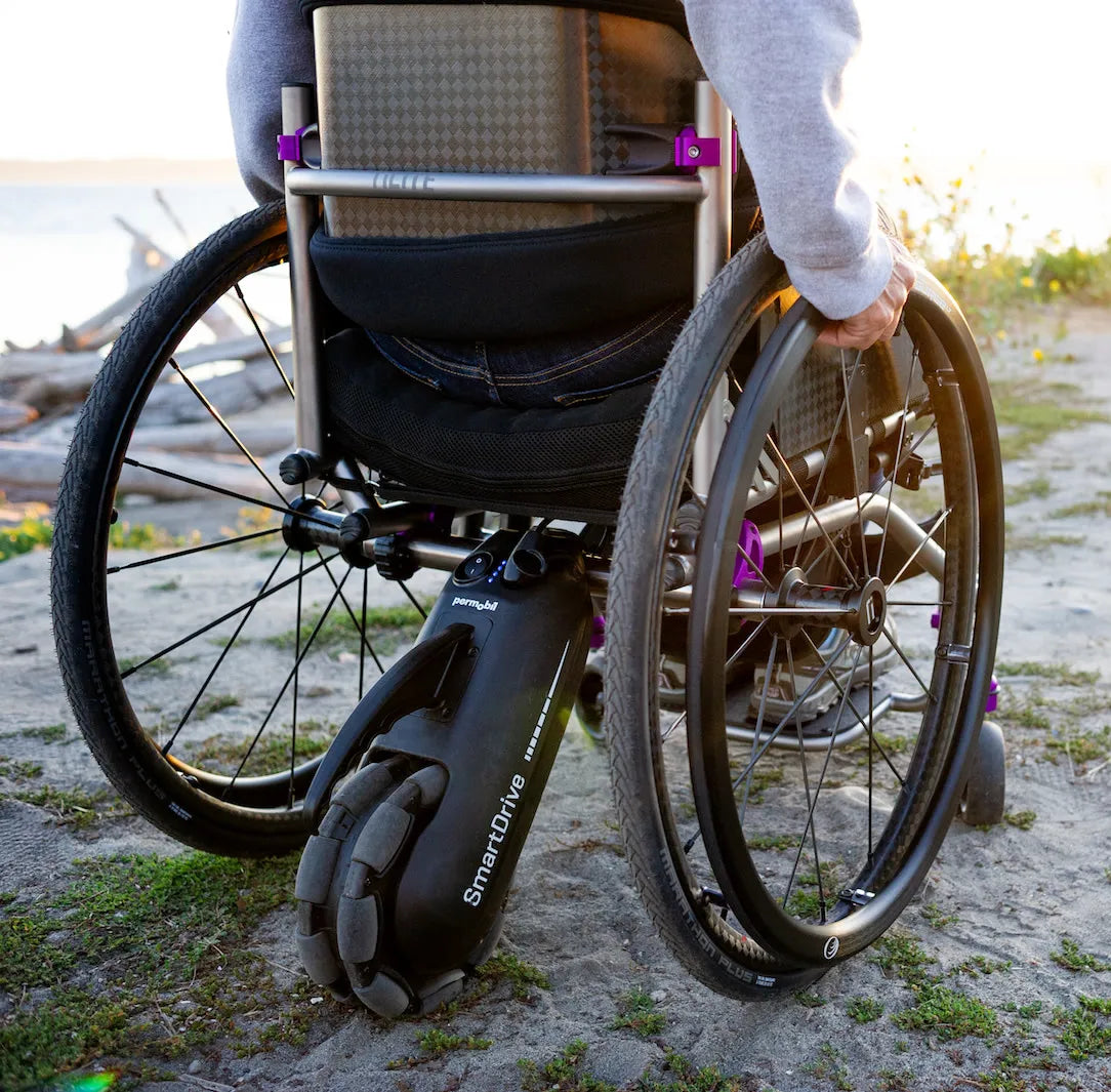A power assist drive unit mounted under a manual wheelchair on a sandy path