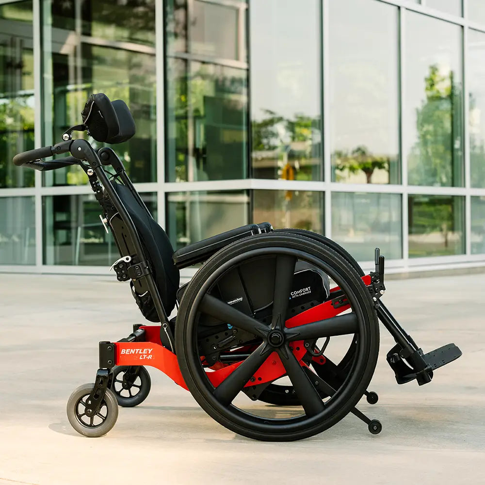 A tilt-in-space manual wheelchair with a headrest outside a glass building