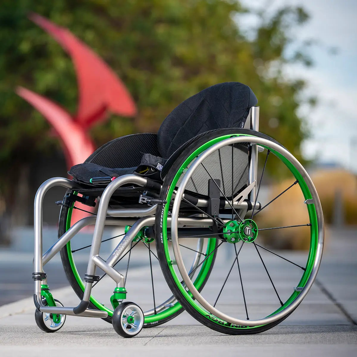 An ultra lightweight manual wheelchair with green wheels outdoors