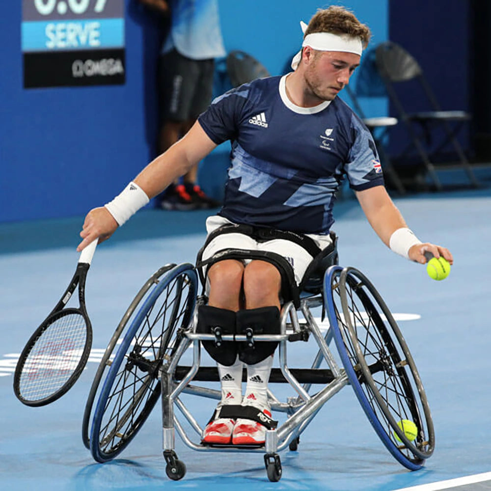 A wheelchair tennis player reaching low for a ball on a blue court