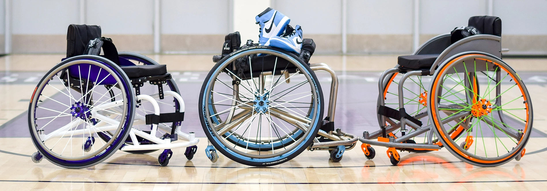Three sport wheelchairs with angled wheels lined up on a gym court