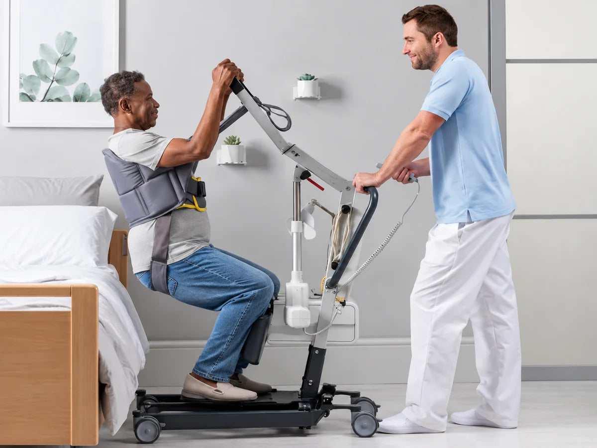 A caregiver helping a man rise from the edge of his bed with a sit-to-stand lift