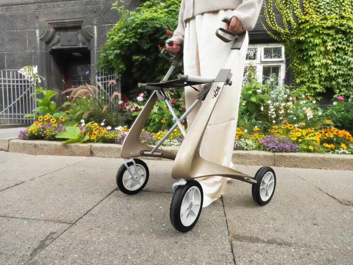 A person walking with a lightweight rollator along a garden sidewalk