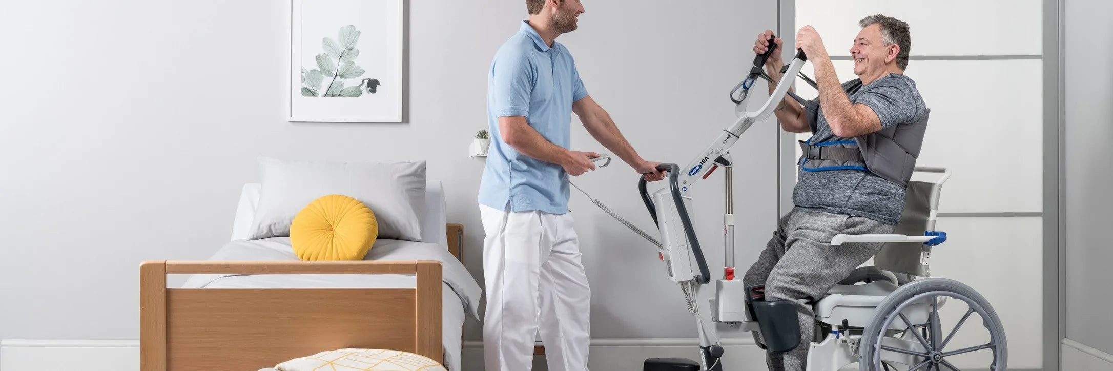 A caregiver helping a man stand from a wheelchair with a stand-up lift beside a bed