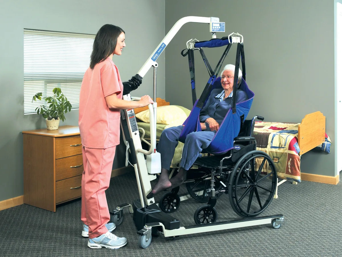 A caregiver lowering a woman in a full body sling into a wheelchair with an electric patient lift
