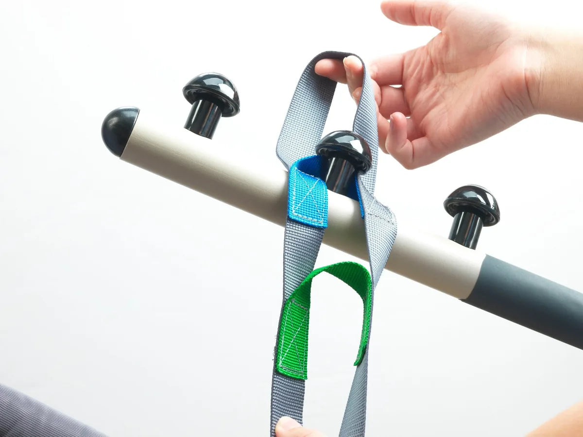 A caregiver hooking a sling strap onto the hooks of a lift spreader bar