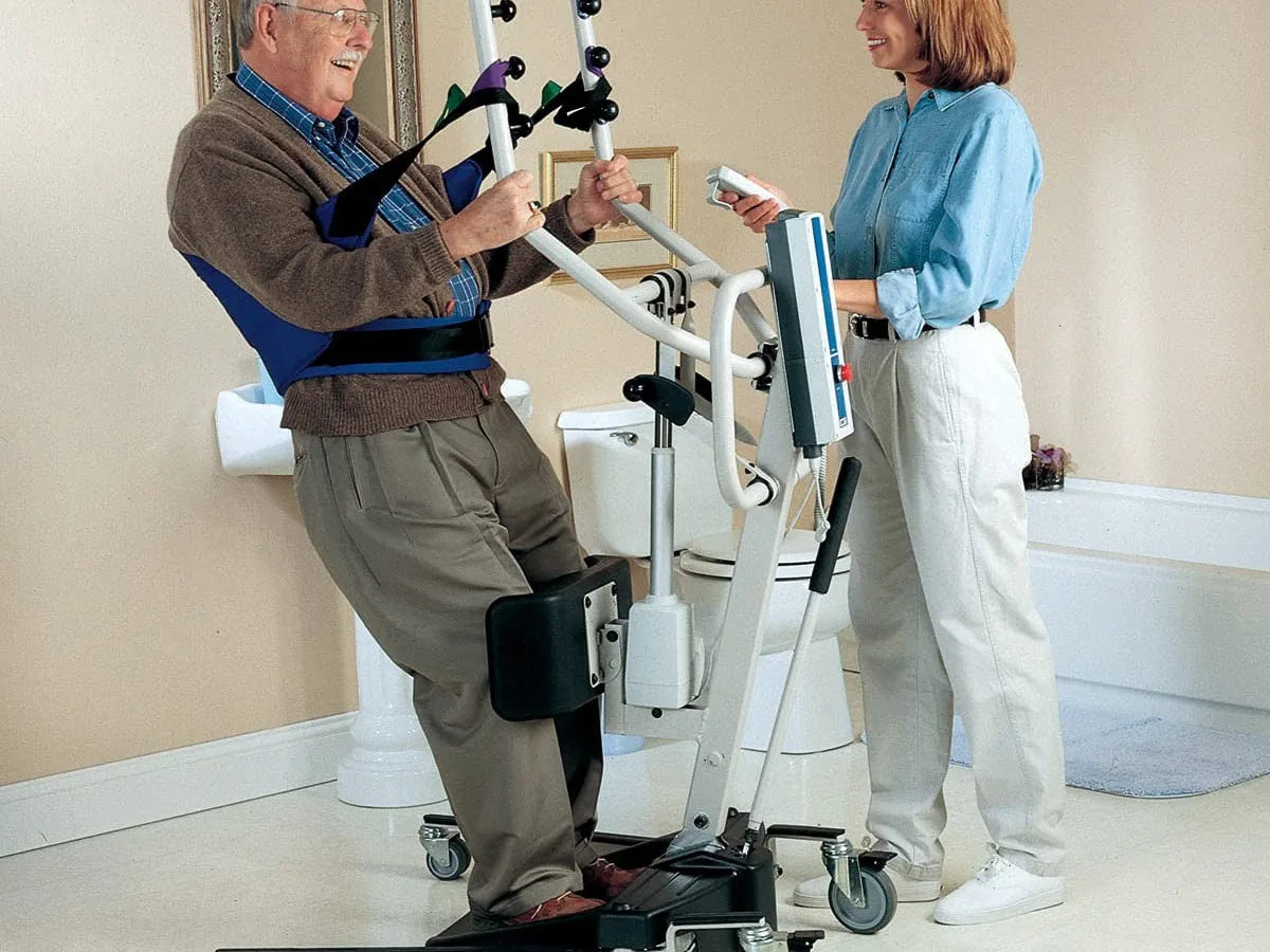 A caregiver helping a man rise to standing with a stand-up lift and a standing sling
