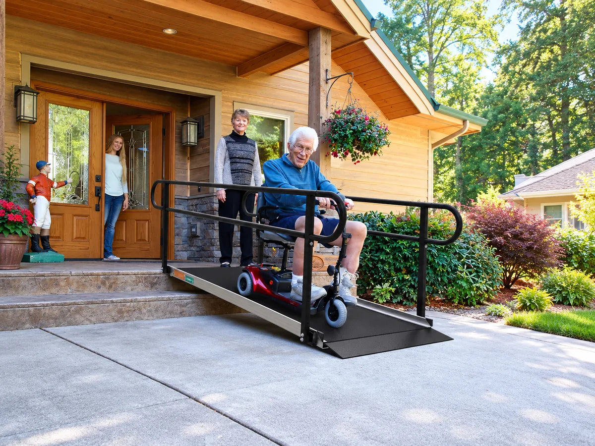 A man on a mobility scooter coming down a ramp with handrails from his front porch as his family watches