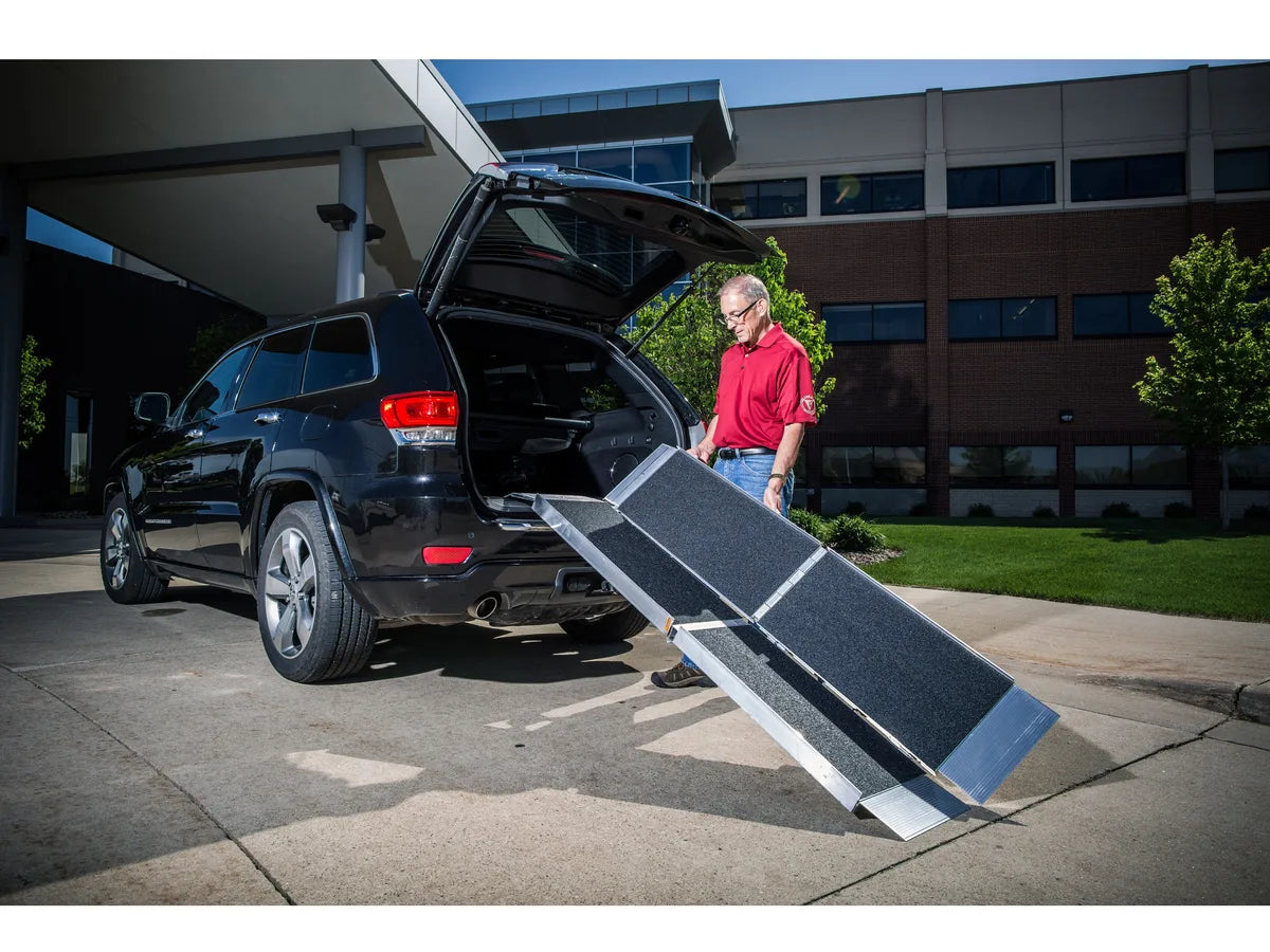 A man unfolding a trifold ramp at the back of an SUV
