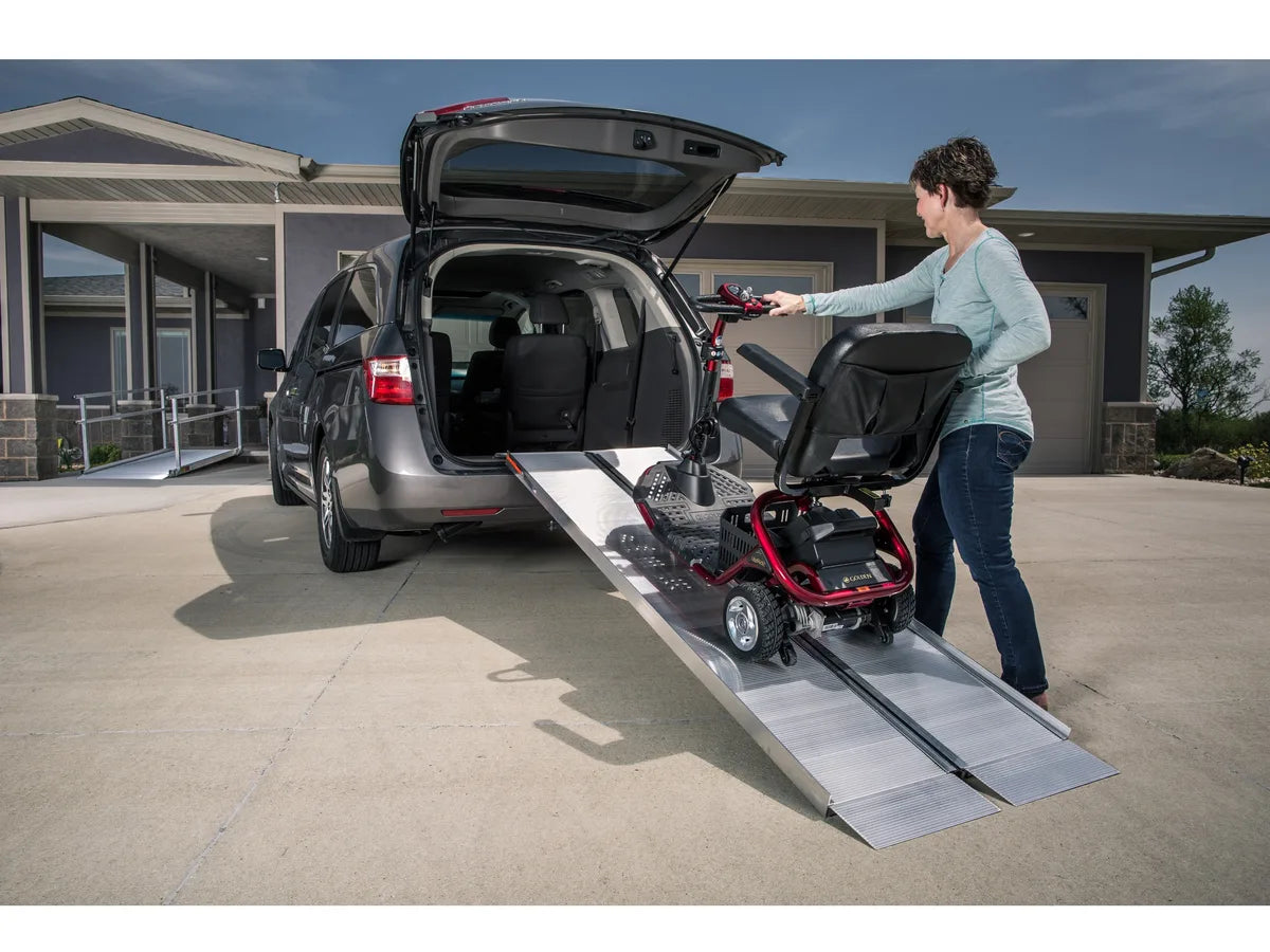 A woman rolling a mobility scooter up a folding ramp into the back of a minivan