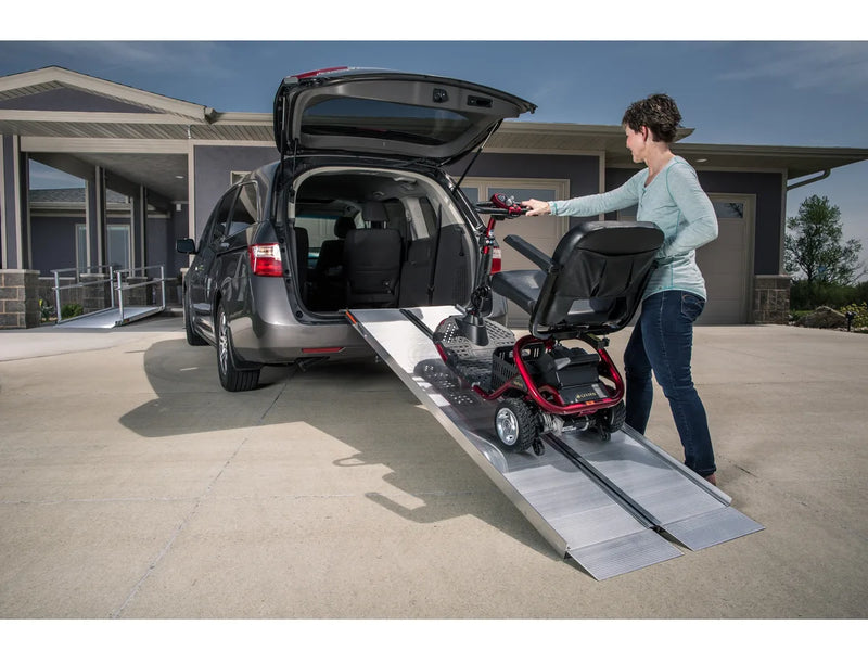 A woman rolling a mobility scooter up a folding ramp into the back of a minivan