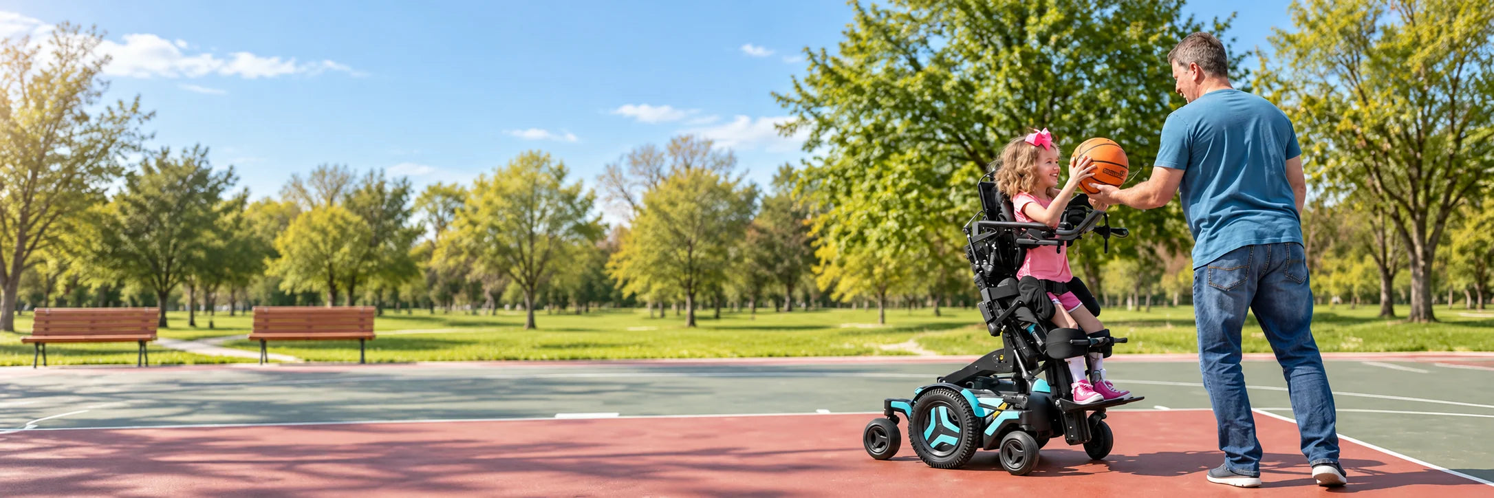 A girl in a power standing wheelchair catches a basketball from her father on an outdoor court in a park