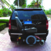 Harmar-AL580_Installed_Straighton_WithChair_lpr Harmar AL580 Power Wheelchair Lift securely mounted to a vehicle, transporting a mid-wheel drive powerchair with a padded hold-down bar.