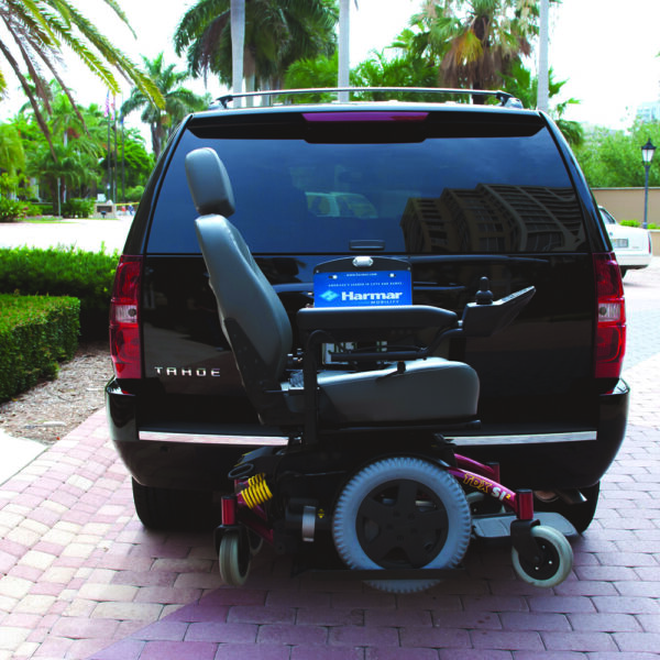 Harmar AL580 Power Wheelchair Lift securely mounted to a vehicle, transporting a mid-wheel drive powerchair with a padded hold-down bar.