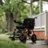 GoRide 2 Electric Wheelchair in orange, foldable aluminum frame, padded seat, 12” rear wheels, and ergonomic joystick controls.